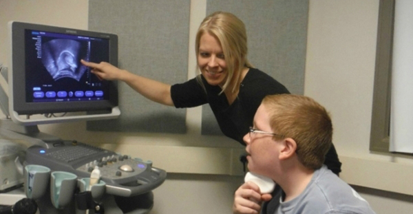 Adolescent holding ultrasound device to throat watching result on screen.